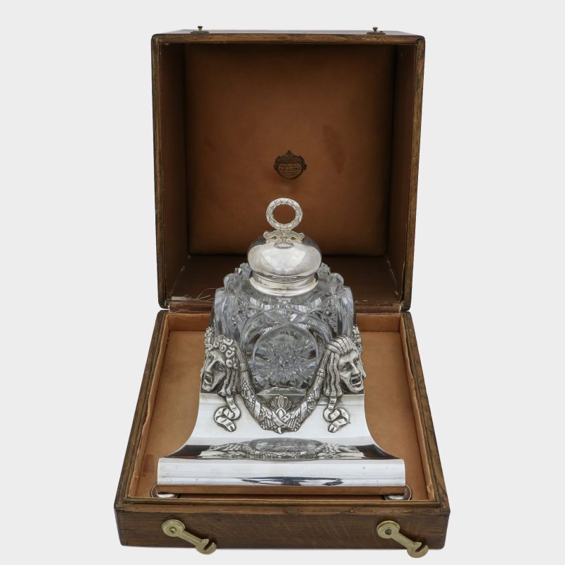 Faberge cut-glass inkwell on trapezoid form silver stand behind front corners cast with theatrical masks, in original box