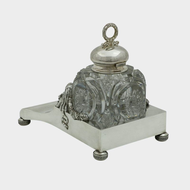 rear view on Faberge inkwell, cut-glass inkwell on trapezoid form silver stand, front corners cast with theatrical masks