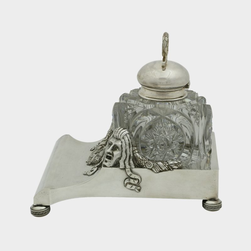 side view on Faberge inkwell, cut-glass inkwell on trapezoid form silver stand, front corners cast with theatrical masks