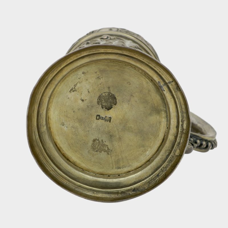 bottom of silver mug with lid decorated with scrolling foliage on stippled grounds