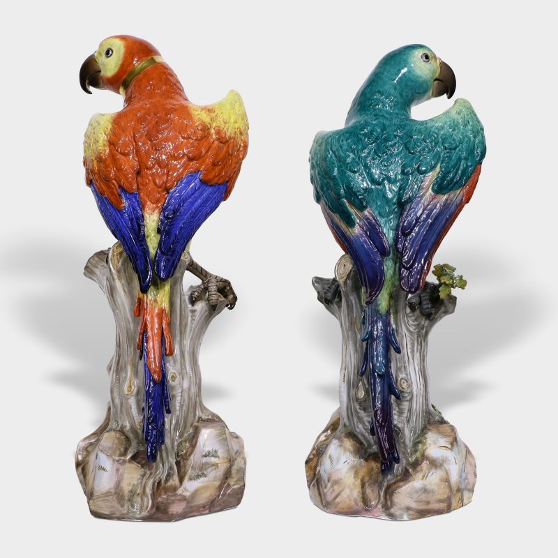 Pair of Meissen porcelain parrots naturalistically modeled with brightly colored plumage perched on tree stump with leaves