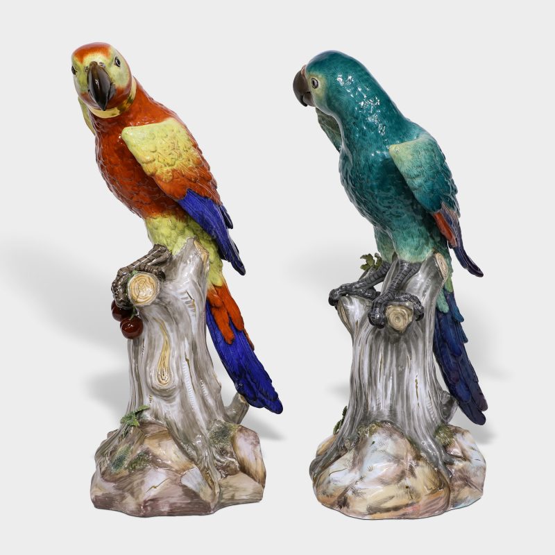 Pair of Meissen porcelain parrots naturalistically modeled with brightly colored plumage perched on tree stump with leaves